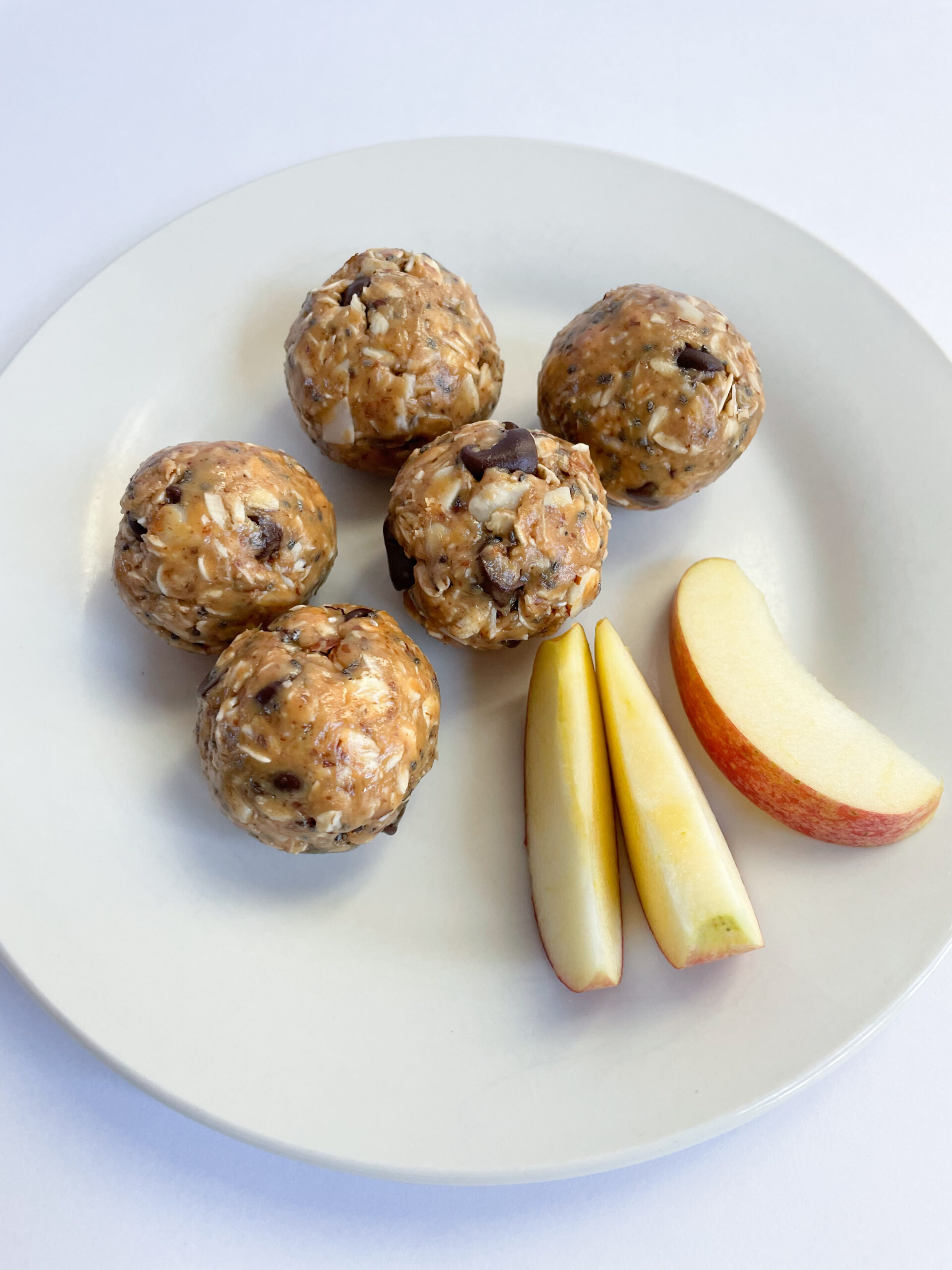 five peanut butter energy bites with three pieces of apple on a white plate.