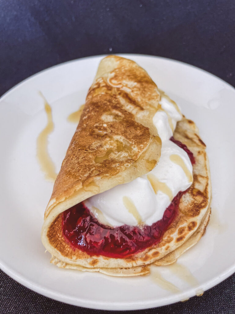 pancake with raspberry jam and homemade whipped cream with maple syrup on a white plate