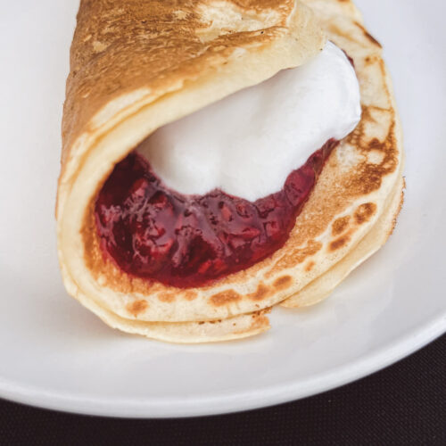 pancake with raspberry jam and homemade whipped cream on a white plate