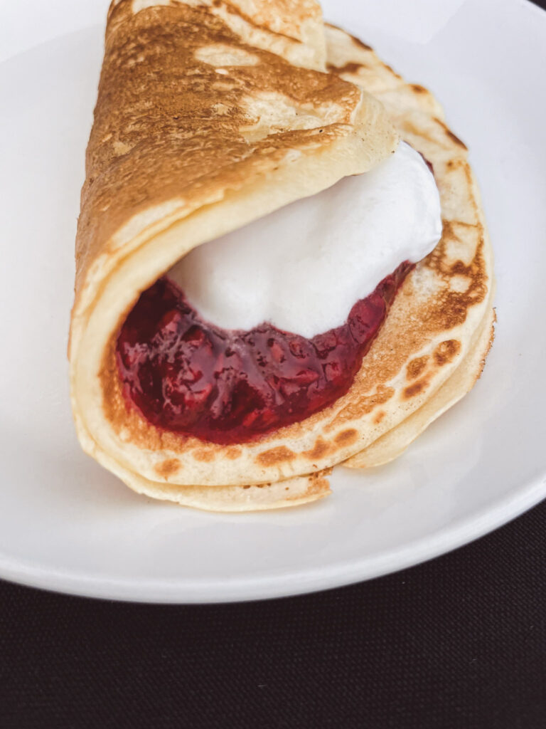 pancake with raspberry jam and homemade whipped cream on a white plate