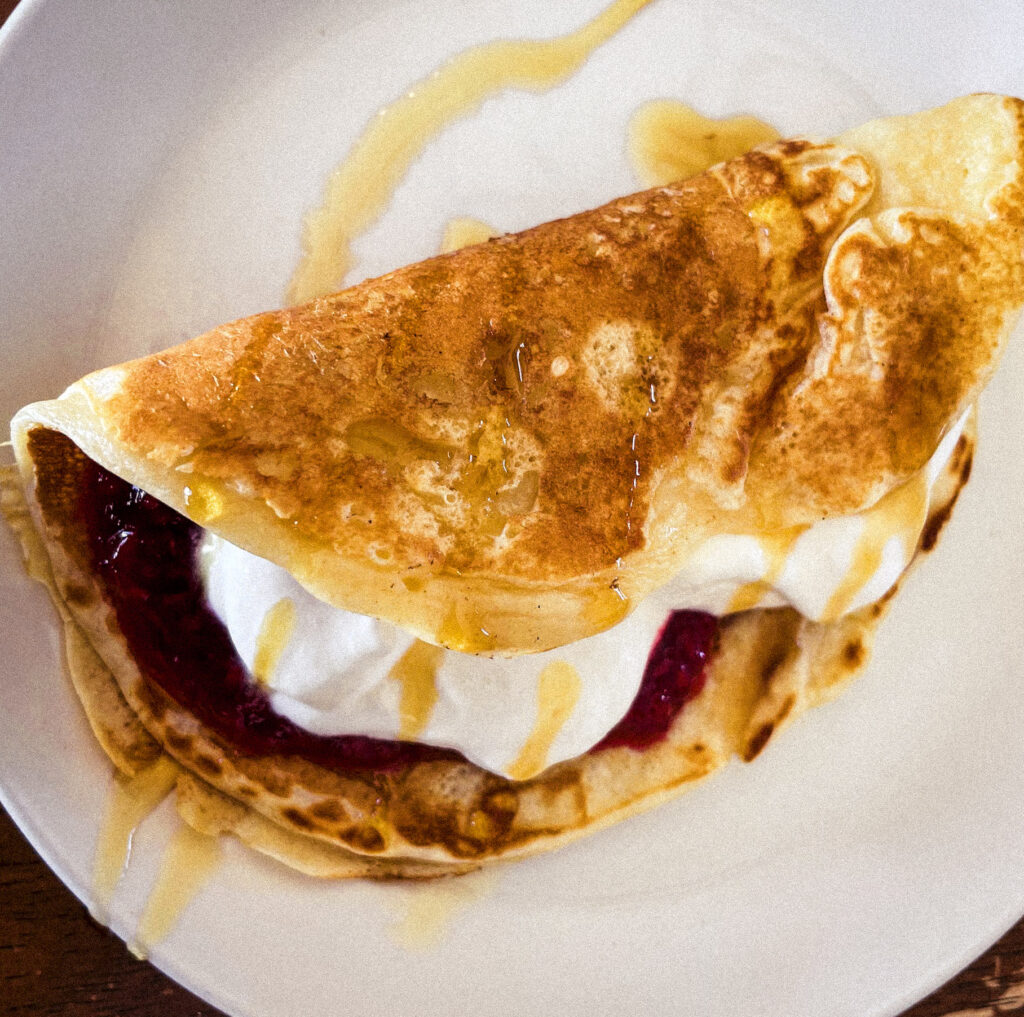 golden brown pancake filled with homemade whipped cream and raspberry jam and drizzled with maple syrup on a white plate